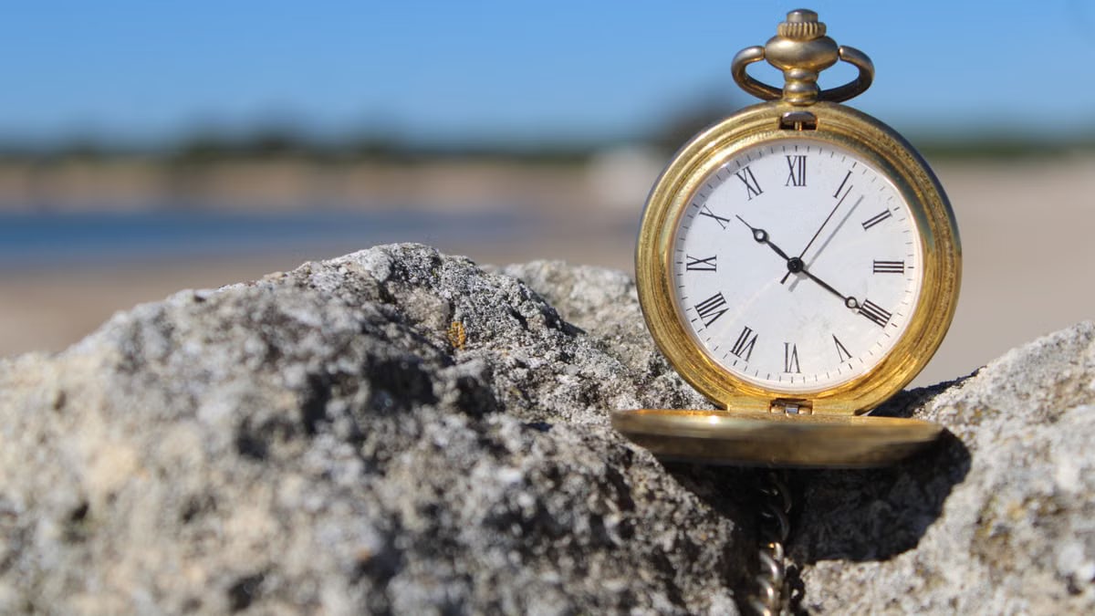 A classic pocket watch resting on beach rocks, capturing timeless elegance under a clear blue sky.
